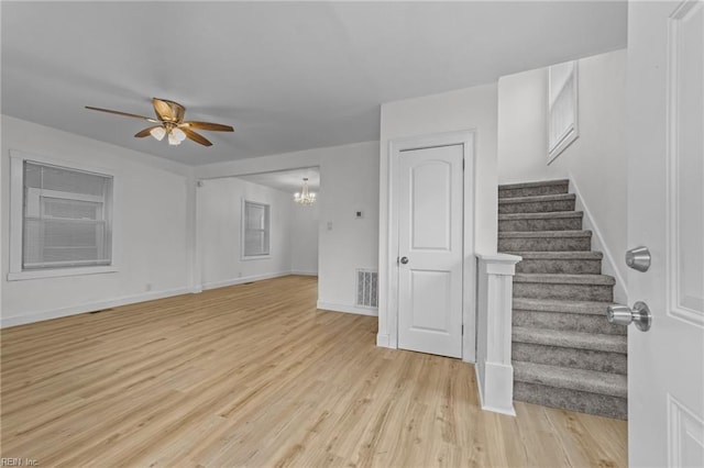 unfurnished living room with visible vents, baseboards, stairs, light wood-style floors, and ceiling fan with notable chandelier