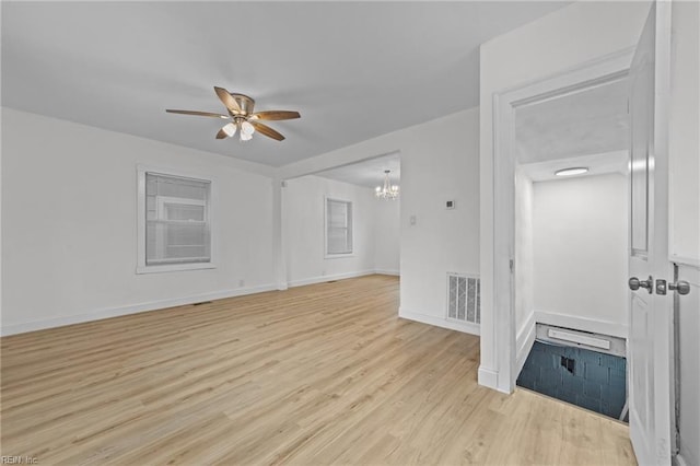 empty room with visible vents, ceiling fan with notable chandelier, light wood-type flooring, and baseboards