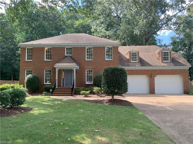 colonial home featuring brick siding, a front yard, roof with shingles, a garage, and driveway