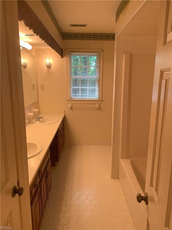 bathroom featuring a sink, visible vents, a bathtub, and double vanity