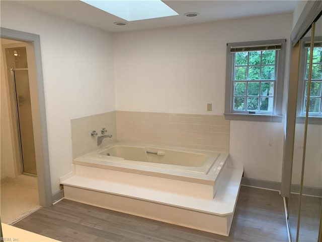 bathroom with baseboards, a garden tub, a stall shower, a skylight, and wood finished floors