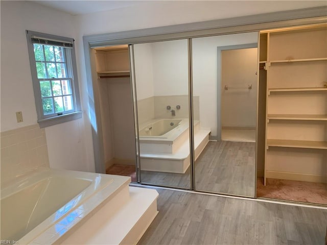 bathroom featuring a walk in closet, a garden tub, and wood finished floors