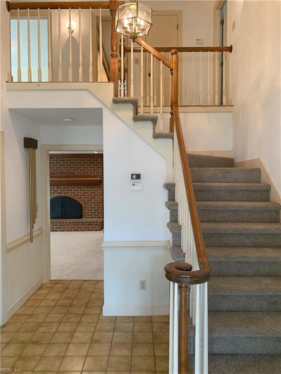 stairs with baseboards, carpet floors, tile patterned flooring, a towering ceiling, and a brick fireplace