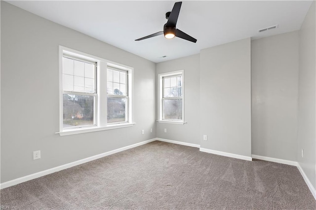 carpeted empty room featuring visible vents, a ceiling fan, and baseboards