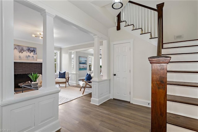 interior space featuring visible vents, wood finished floors, a fireplace, crown molding, and decorative columns