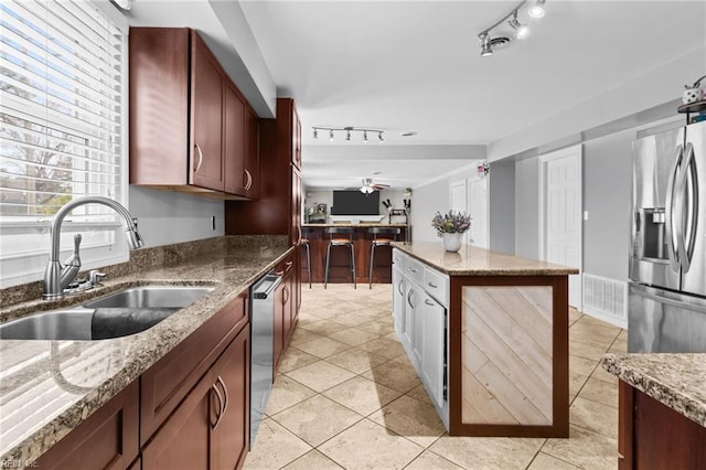 kitchen with a sink, a kitchen island, appliances with stainless steel finishes, stone counters, and light tile patterned floors