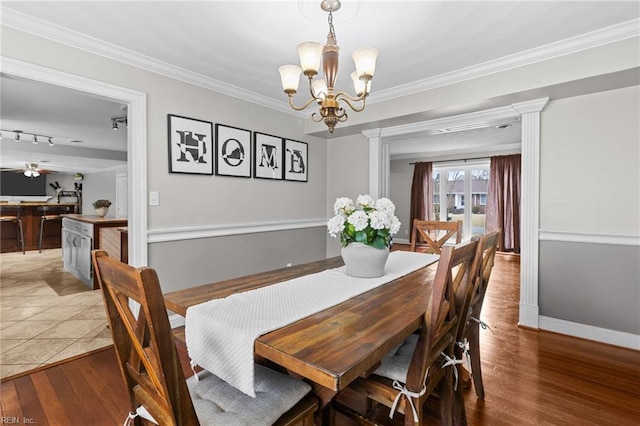 dining room with baseboards, ornamental molding, ceiling fan with notable chandelier, wood finished floors, and ornate columns