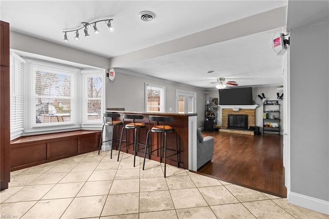 kitchen featuring visible vents, a kitchen bar, tile patterned flooring, a brick fireplace, and ceiling fan