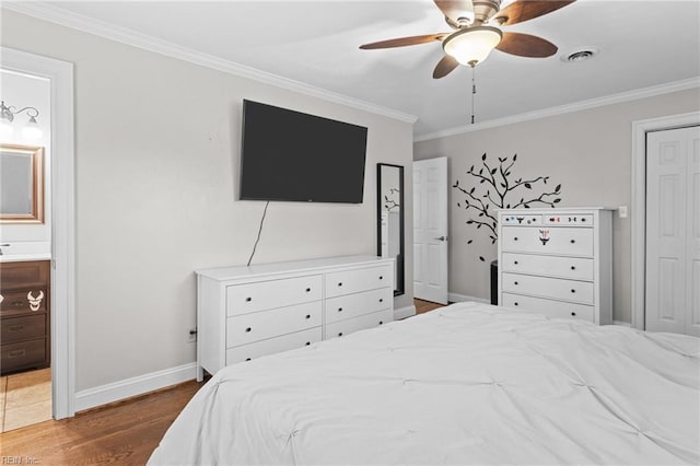 bedroom featuring visible vents, crown molding, baseboards, ensuite bathroom, and wood finished floors