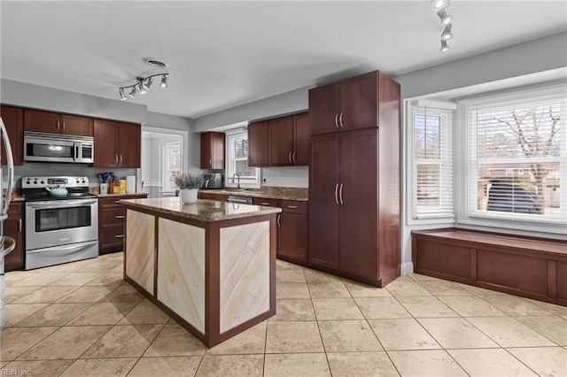 kitchen featuring light tile patterned floors, a kitchen island, dark stone counters, a sink, and stainless steel appliances