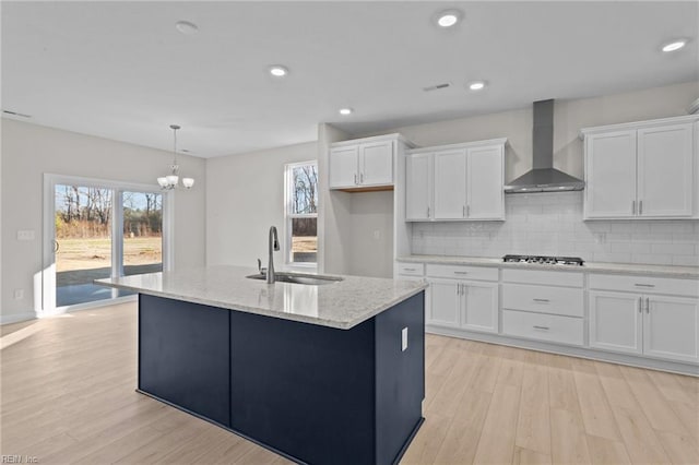 kitchen featuring white cabinetry, light wood-type flooring, wall chimney range hood, and a sink