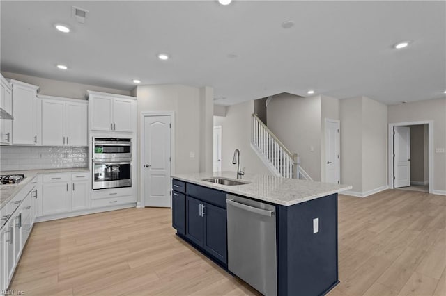 kitchen featuring light wood finished floors, backsplash, appliances with stainless steel finishes, white cabinetry, and a sink