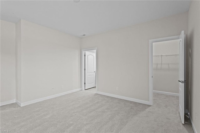 unfurnished bedroom featuring a closet, a walk in closet, baseboards, and carpet floors