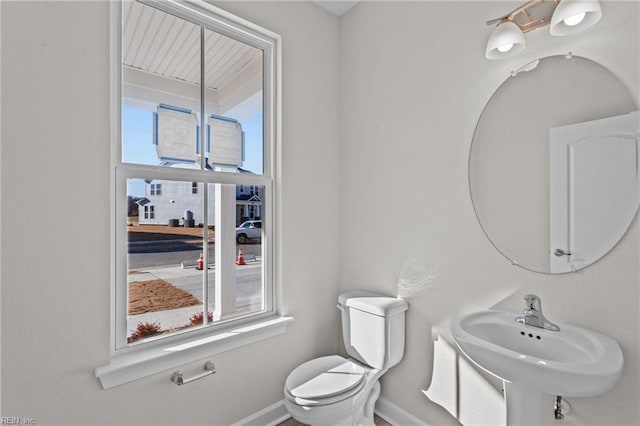 bathroom featuring a sink, baseboards, toilet, and a healthy amount of sunlight