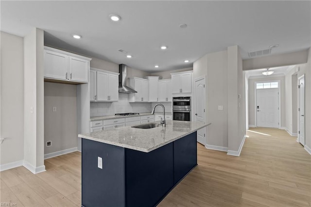 kitchen featuring visible vents, a sink, cooktop, white cabinets, and wall chimney range hood