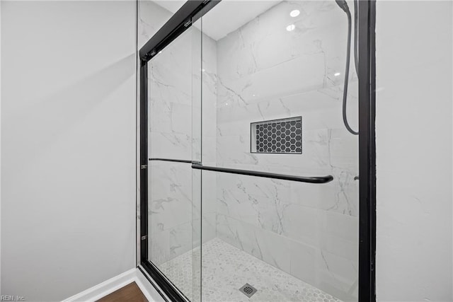 full bath with a marble finish shower, baseboards, and wood finished floors