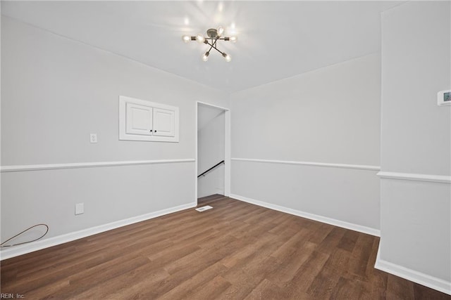 empty room featuring baseboards, wood finished floors, visible vents, and a chandelier