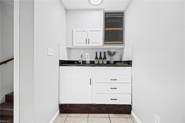 bar featuring baseboards, light tile patterned floors, decorative backsplash, indoor wet bar, and a sink