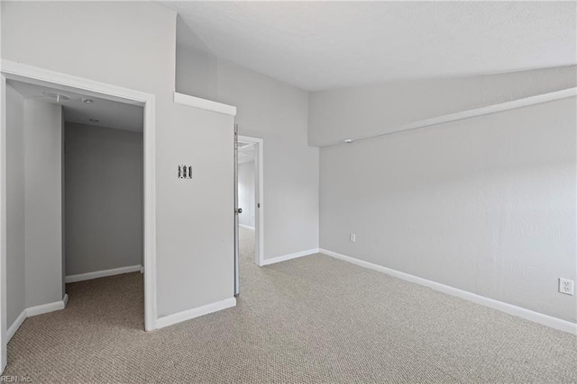 carpeted empty room featuring baseboards and vaulted ceiling