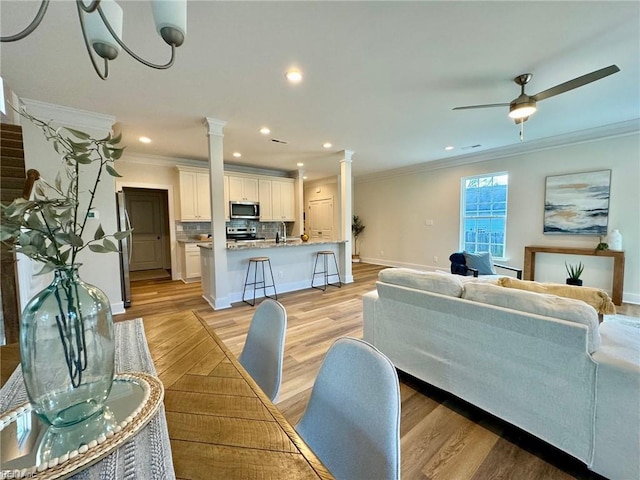 living area with light wood-style flooring, crown molding, baseboards, and decorative columns