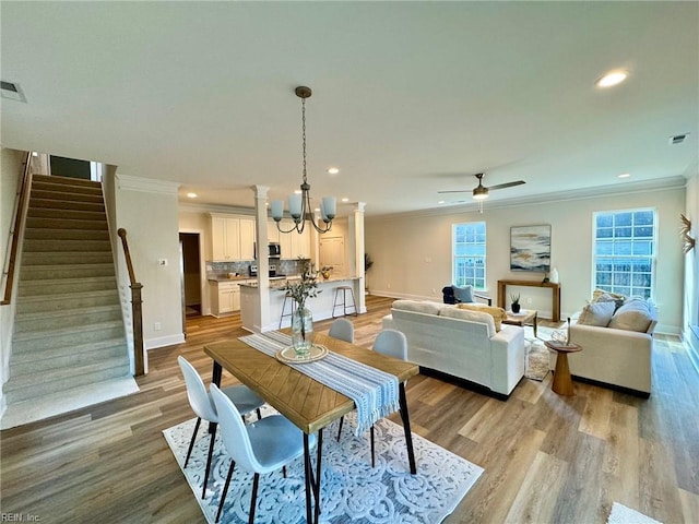 dining space with light wood-style flooring, stairway, ornamental molding, and ceiling fan with notable chandelier