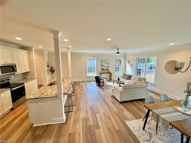 living room with a ceiling fan, baseboards, light wood finished floors, ornate columns, and crown molding