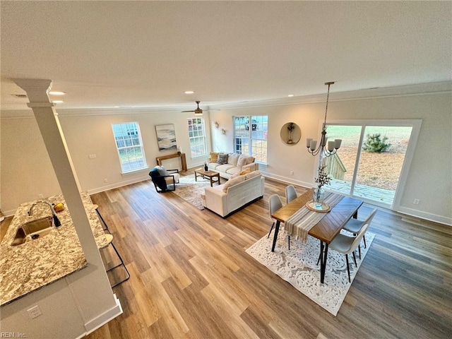 living room featuring light wood-type flooring, baseboards, crown molding, and ornate columns