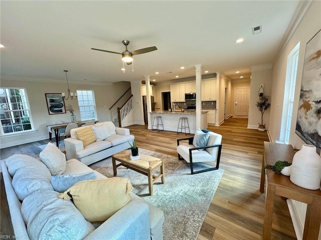 living area featuring visible vents, stairway, light wood-type flooring, and ornamental molding