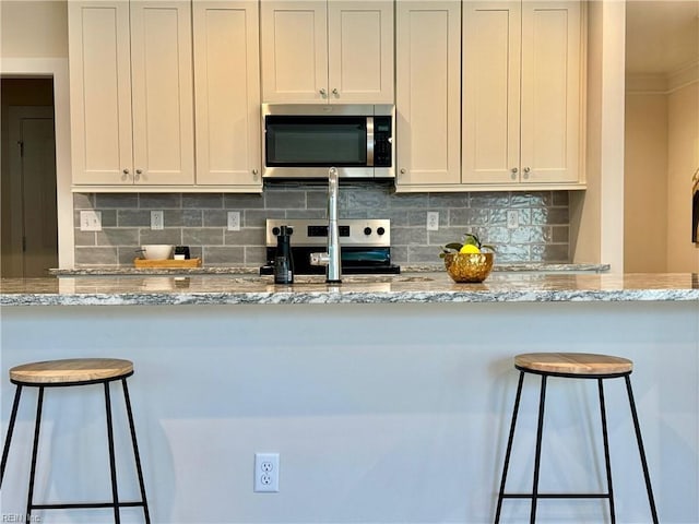 kitchen featuring light stone counters, decorative backsplash, stainless steel appliances, and a breakfast bar