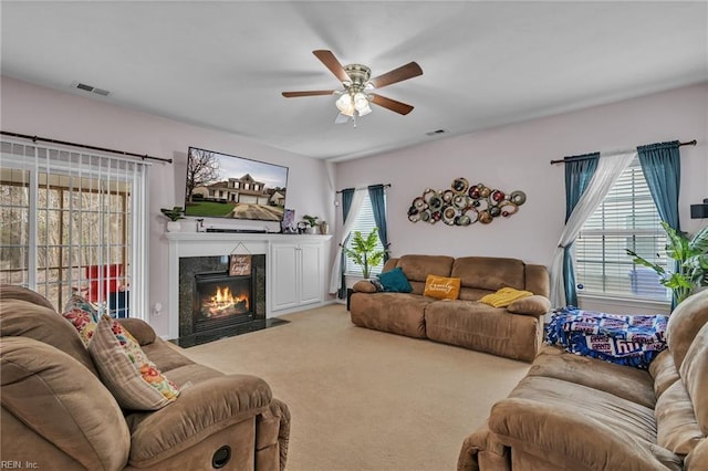 carpeted living room featuring visible vents, plenty of natural light, a high end fireplace, and a ceiling fan