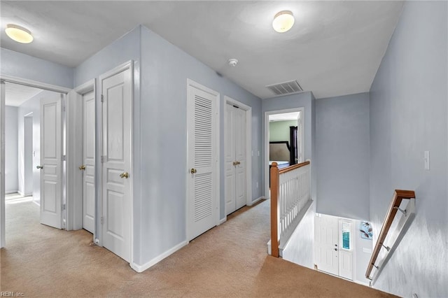 hall featuring visible vents, an upstairs landing, carpet, and baseboards