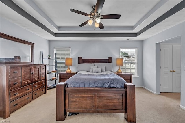 bedroom featuring baseboards, a raised ceiling, light colored carpet, and ceiling fan