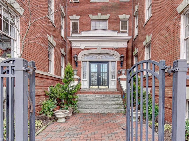 doorway to property featuring french doors, fence, brick siding, and a gate