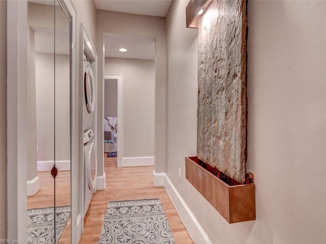 corridor with wood finished floors, stacked washer and clothes dryer, and baseboards