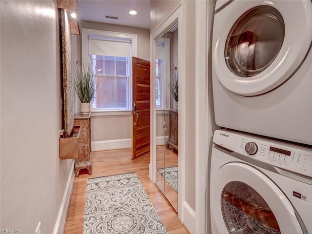 laundry area with visible vents, baseboards, laundry area, stacked washing maching and dryer, and light wood-style floors