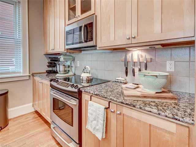 kitchen featuring light stone countertops, light brown cabinets, light wood finished floors, baseboards, and appliances with stainless steel finishes