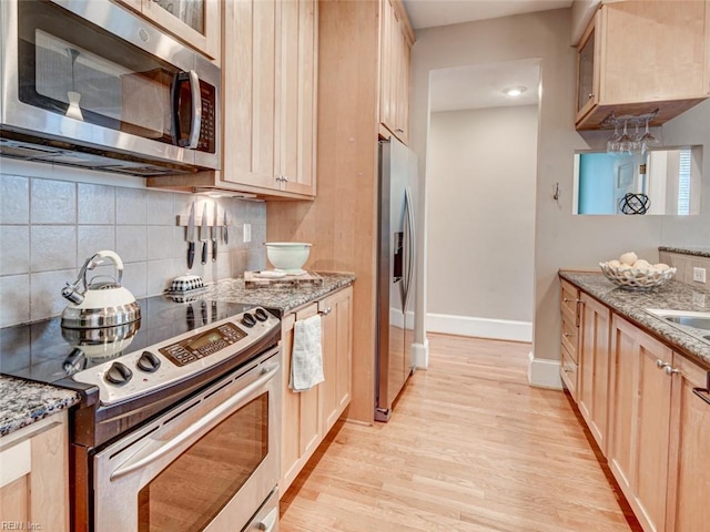 kitchen with light brown cabinets, light stone counters, decorative backsplash, light wood-style flooring, and stainless steel appliances