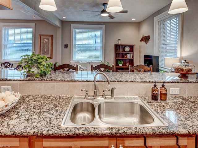 kitchen with a sink, light stone counters, and ceiling fan