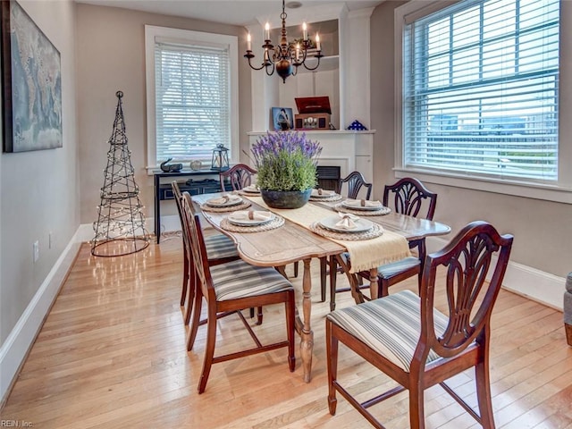 dining room featuring a notable chandelier, a fireplace, light wood-type flooring, and baseboards