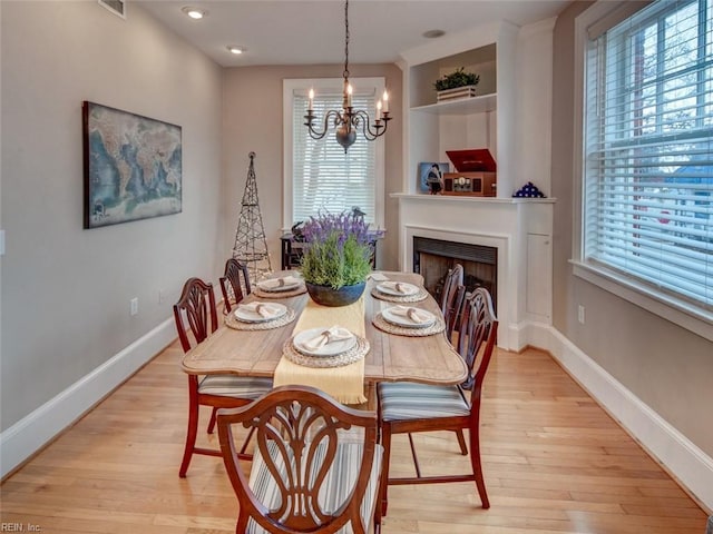 dining area featuring light wood-type flooring, a fireplace, baseboards, and a chandelier