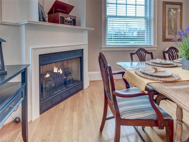 dining space with baseboards, a lit fireplace, and light wood finished floors