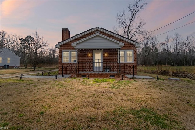 bungalow-style house featuring a yard, brick siding, and a chimney