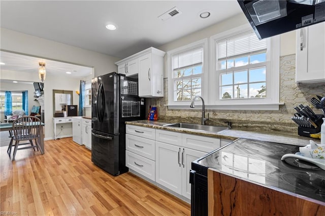 kitchen featuring visible vents, exhaust hood, white cabinets, black appliances, and a sink