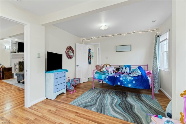 bedroom with visible vents, a fireplace, baseboards, and wood finished floors