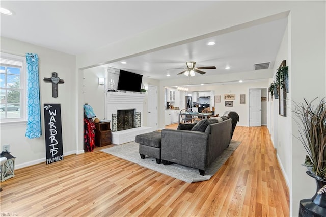 living area featuring visible vents, a fireplace with raised hearth, light wood-type flooring, recessed lighting, and a ceiling fan