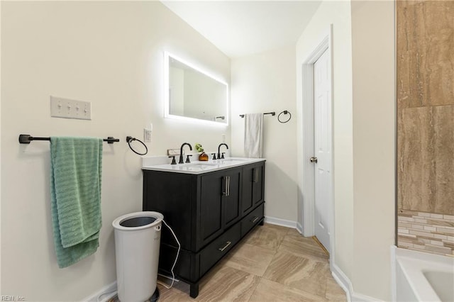 full bath with double vanity, baseboards, a tub, and a sink