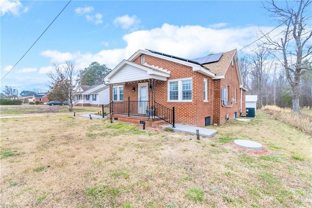 bungalow-style home featuring solar panels, a front lawn, central air condition unit, and brick siding
