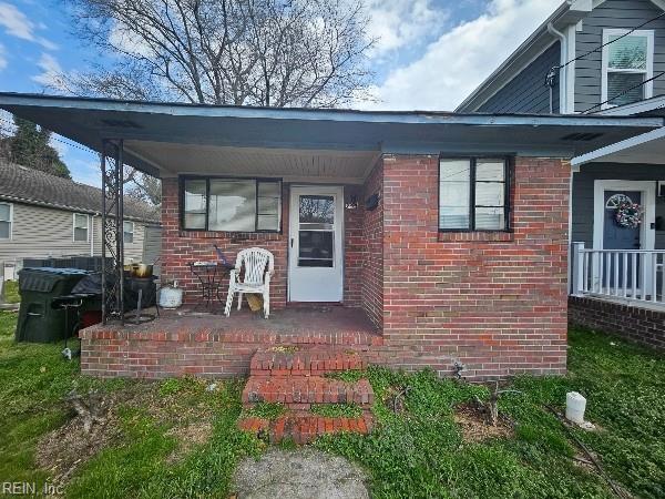 view of exterior entry featuring brick siding and covered porch