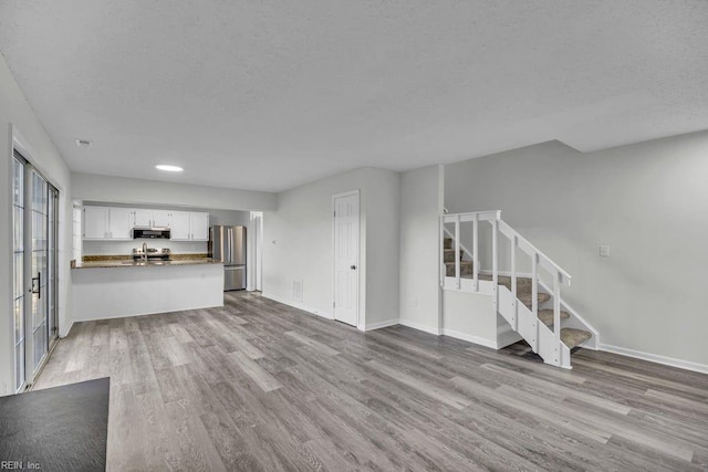 unfurnished living room featuring baseboards, a textured ceiling, wood finished floors, and stairs