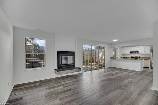 unfurnished living room with wood finished floors, baseboards, a multi sided fireplace, and a sink